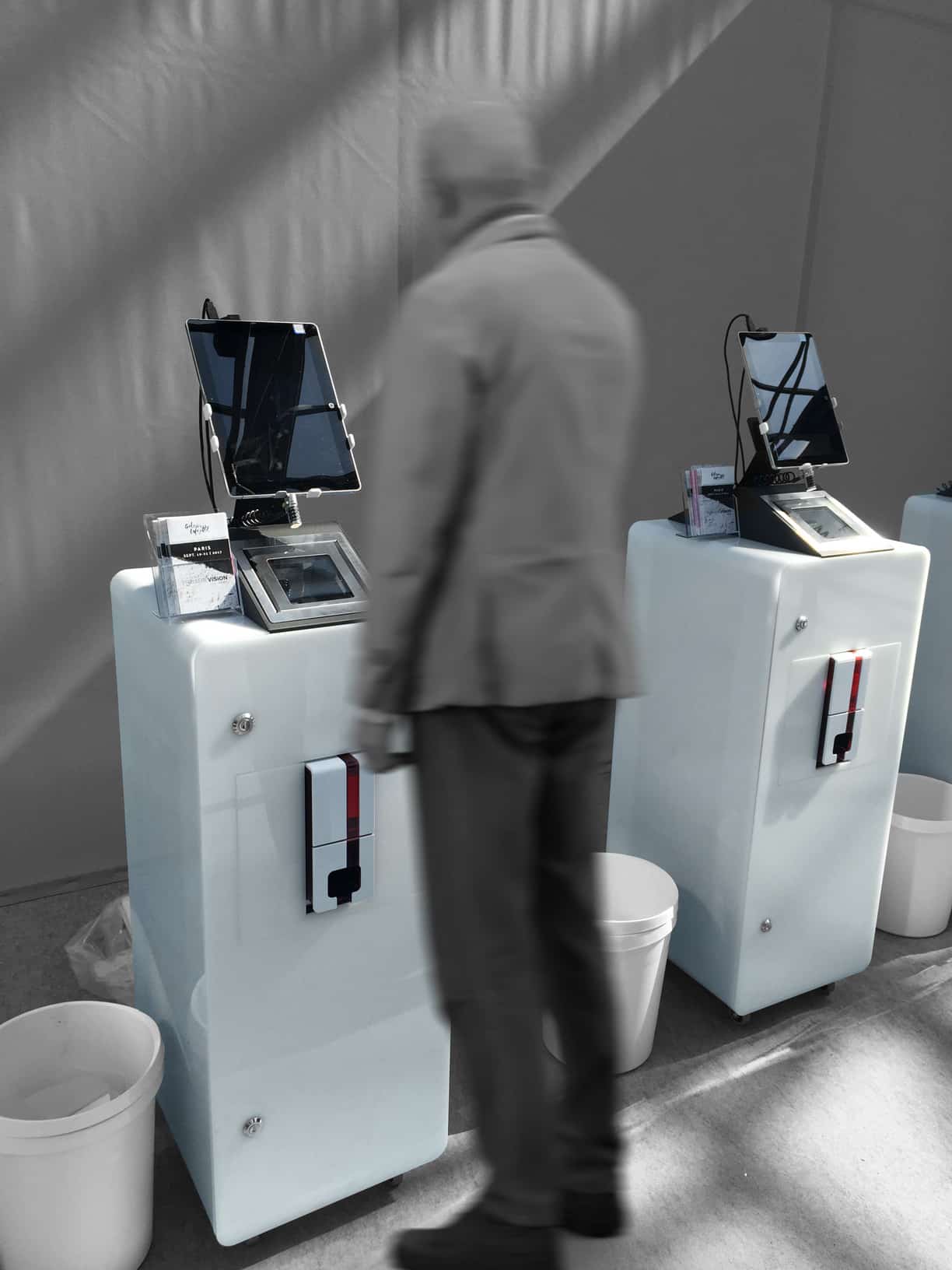 Une personne se tient devant un Borne Tactile dans un cadre moderne et minimaliste, avec deux machines blanches et des paniers à proximité.